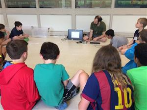kids gather around a man showing them a laptop screen